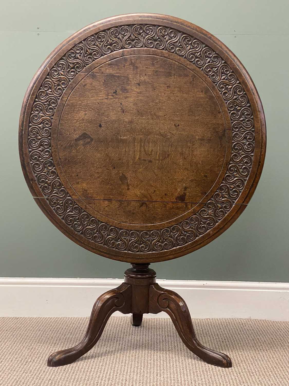 19th century oak tripod table, circular tilt top carved with a band of scrolls within a moulded 19th century oak tripod table, circular tilt top carved with a band of scrolls within a moulded